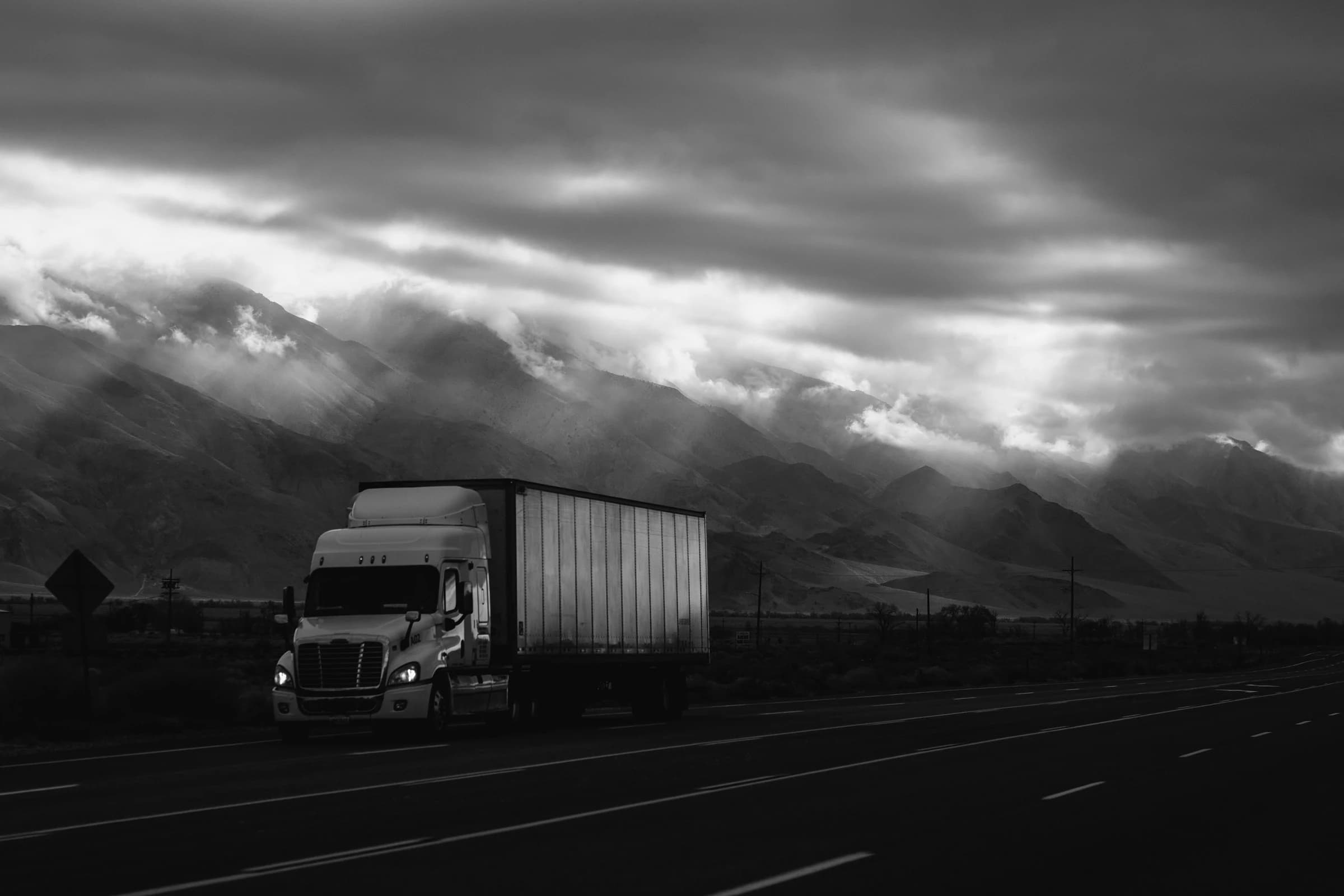 Truck on a highway beneath storm-lit mountains