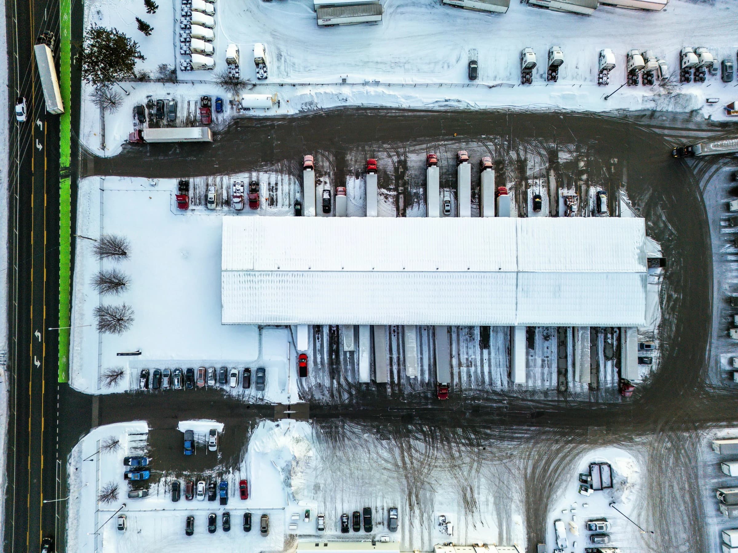 Aerial view of a freight dock in winter — trucks backed to loading bays, snow-covered yard